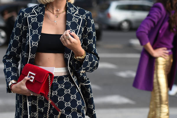 A model at Fashion Week showcases branding trends with a stylish outfit, featuring a logo blazer and red clutch.